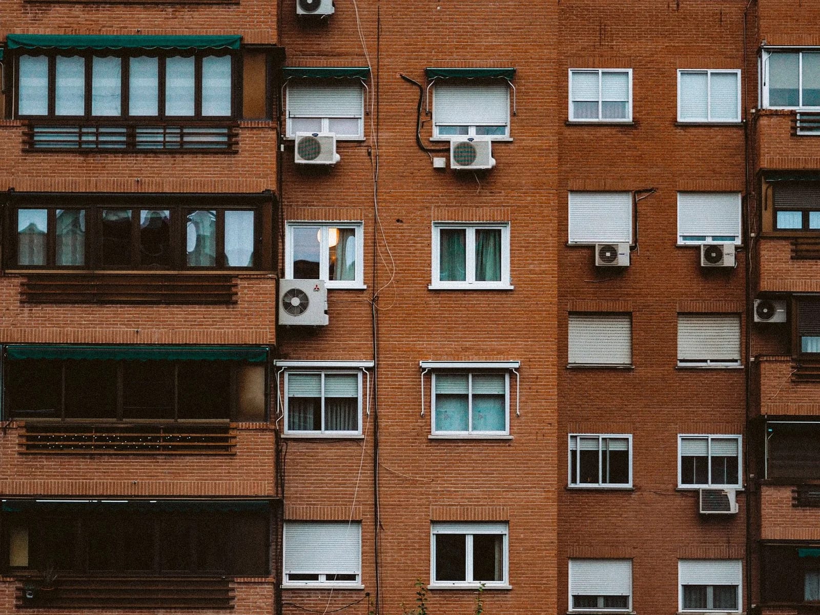 A detailed view of an orange brick apartment facade with windows and air conditioners.